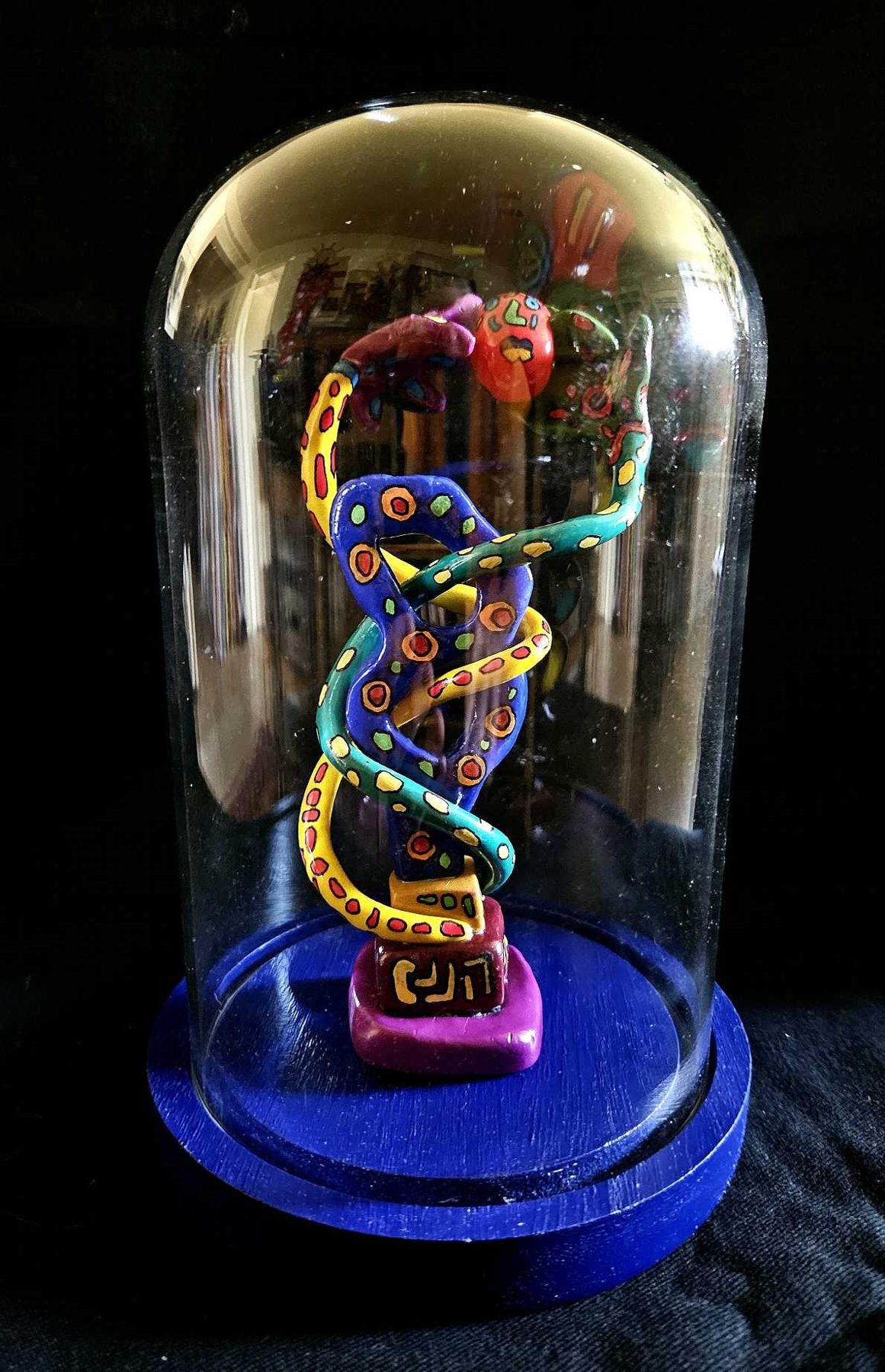 Serpent coloré enroulé sous une cloche de verre sur socle bleu